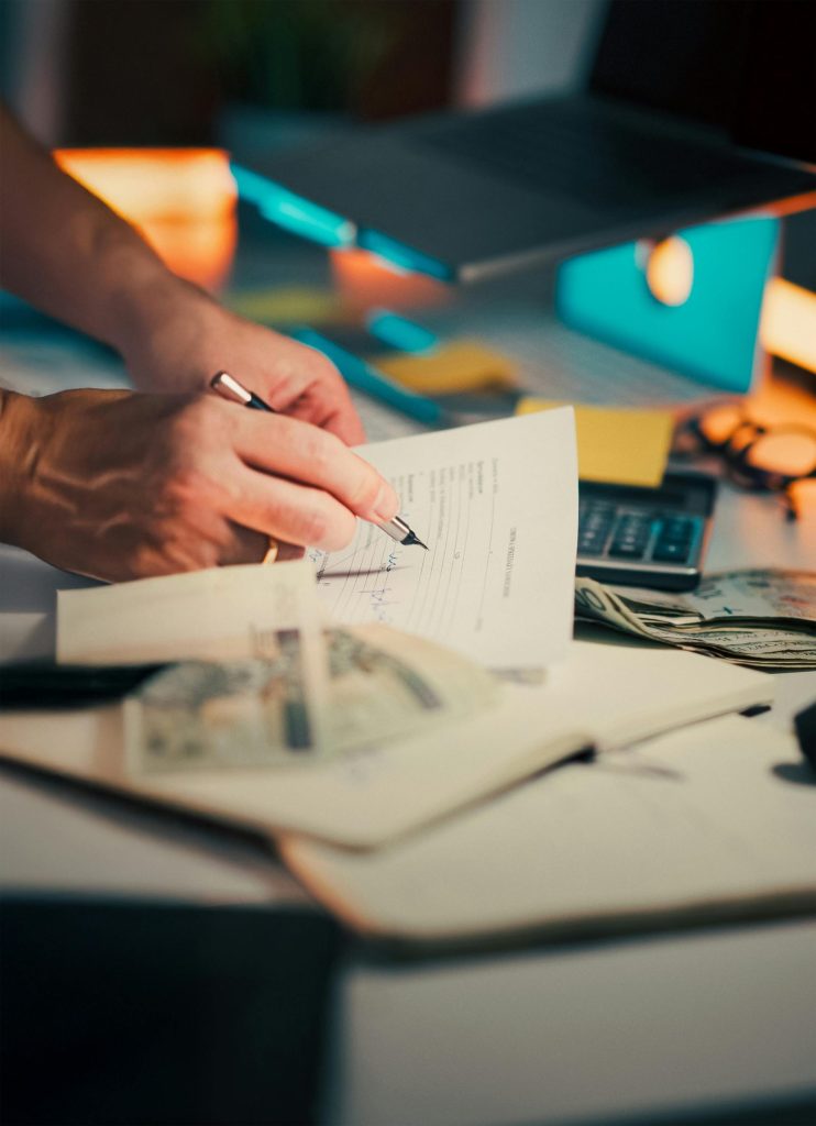 Eine Hand, die auf einem Schreibtisch mit Bargeld und einem Taschenrechner Finanzdokumente unterzeichnet, symbolisiert Finanzmanagement.