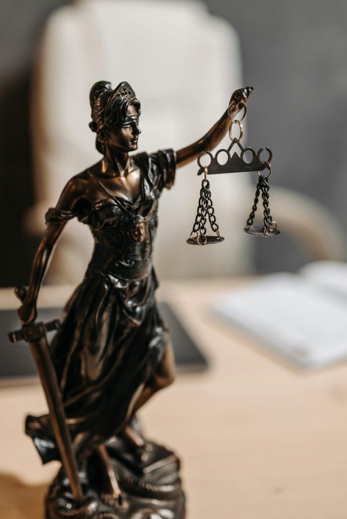 Bronzene Justitia-Statue mit Waage und Schwert, Symbol für Gerechtigkeit und Recht.